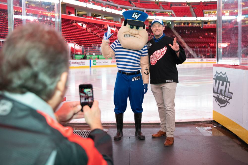 An alumnus posing with Louie the Laker at the Detroit Red Wings GVSU Night